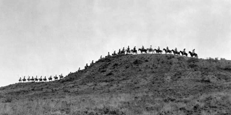 A black and white photo of around 20-30 people on horses on a mountain range.