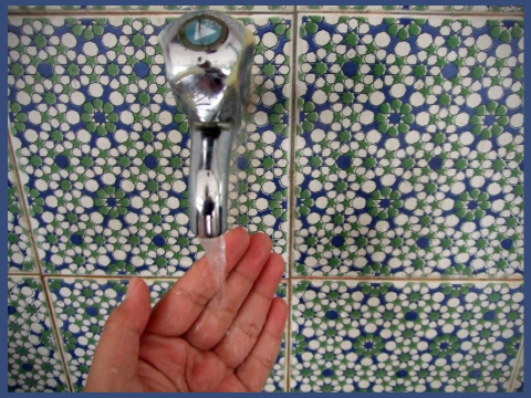 A woman's hand under a faucet with a backdrop of beautiful Islamic tile.