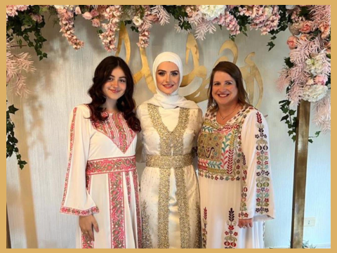 Three women stand smiling for a picture, dressed in white, gold, and light pink dress attire.