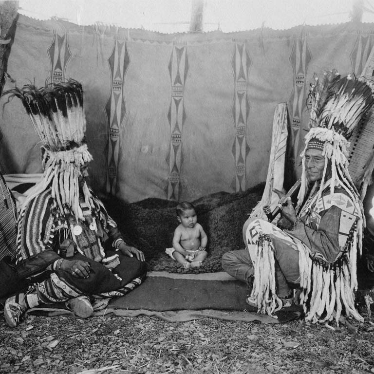 Two individuals in traditional native clothing sitting with a baby sitting in between them