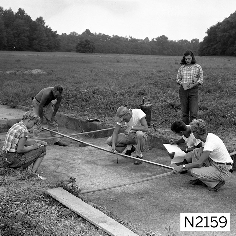 Image of a group of archaeologists measuring a squared space at an excavation.