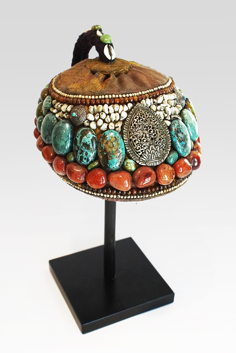 A headpiece decorated with three main rows of semi-precious stones. The lowest row has  red/orange stones, the middle row has speckled blue stones and the top is small white stones. There is a large tear drop pendant in the center of the head piece.
