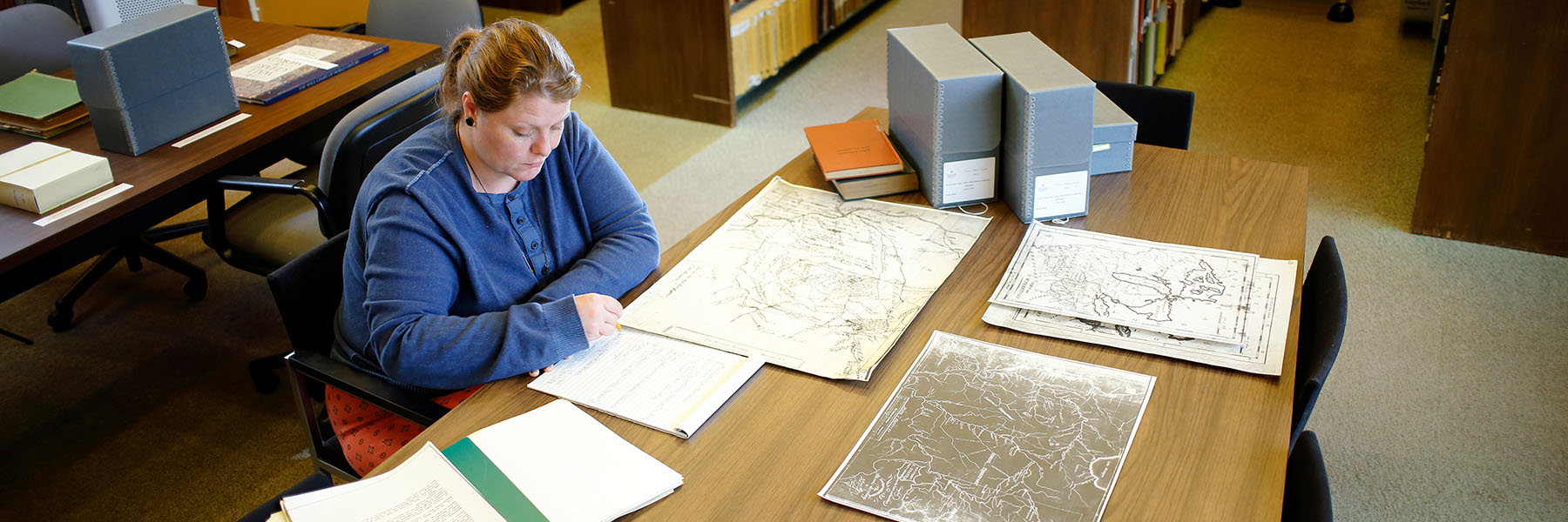 Image of a women sitting at a table looking at maps and documents.