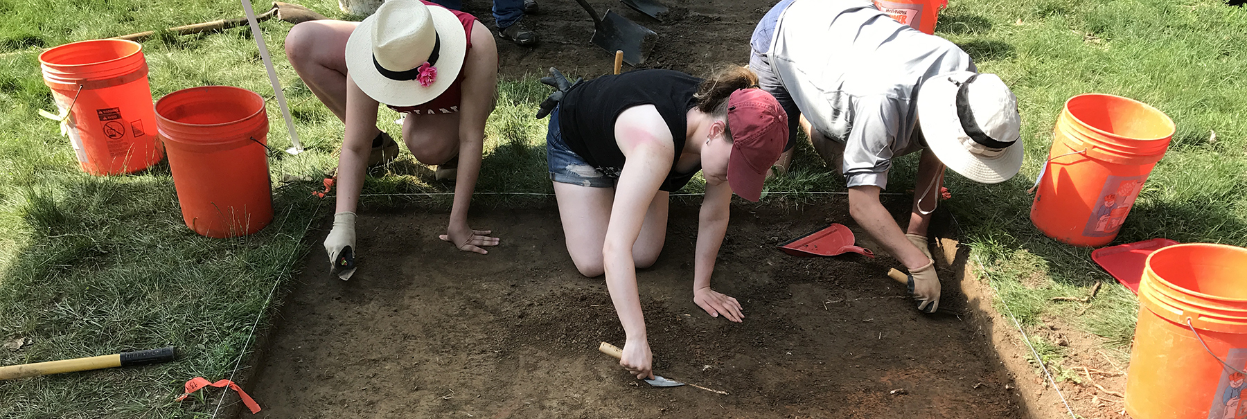An image of three students working in a single square practicing excavation technique. With four orange buckets, two on either side.